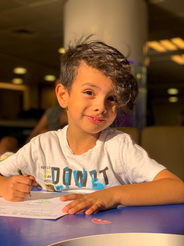 A smiling boy sitting at a table in a busy indoor play area