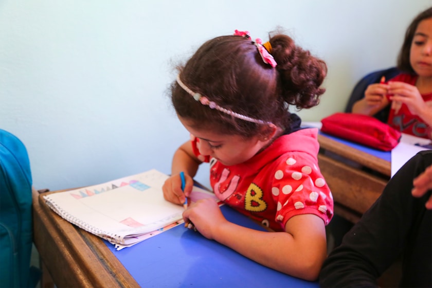 A girl in a headband concentrating on a drawing at her desk