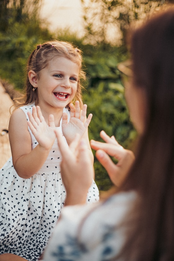 A young girl laughing and signing with her hands while an adult signs back