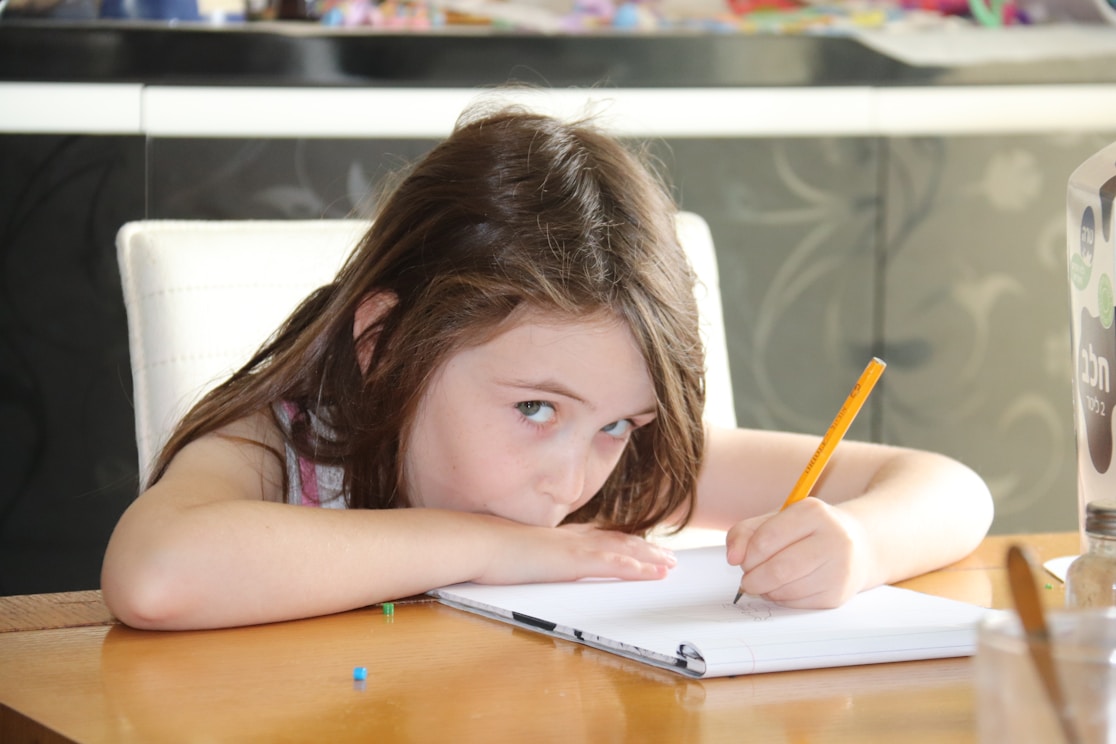 A girl resting her head on a table while writing