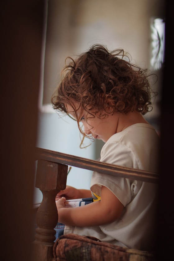 A curly-haired child reading quietly by a wooden railing