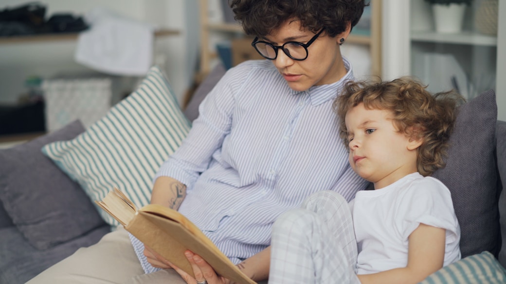 A mother reading a book with her son on the sofa