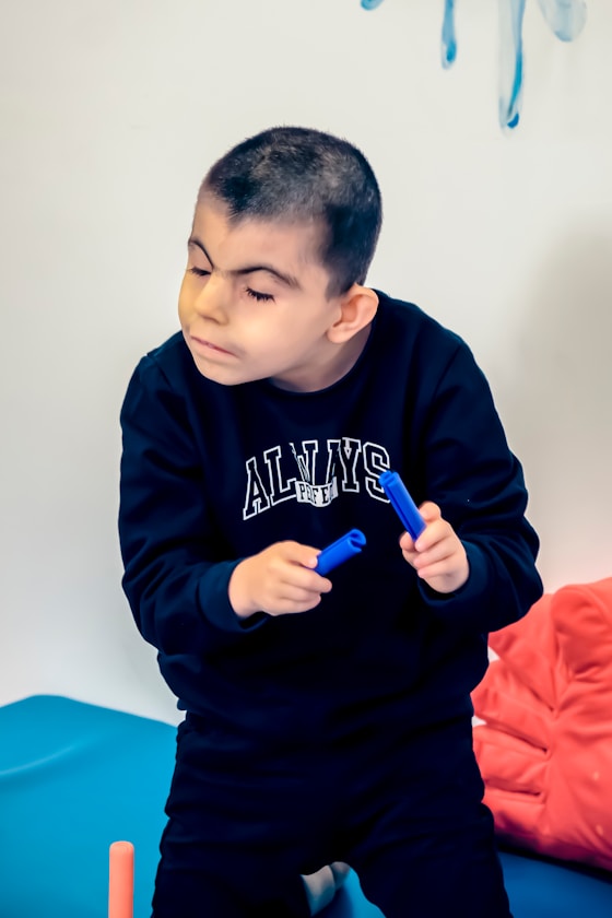 A boy holding two blue toy items, looking down thoughtfully