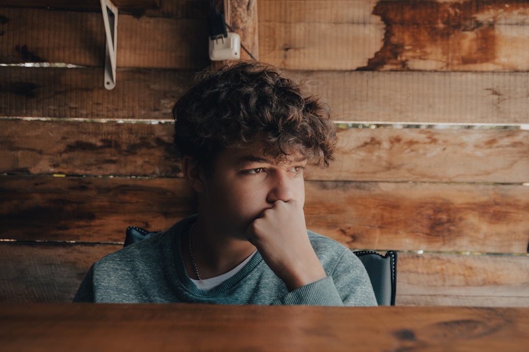 A young man sitting thoughtfully against a wooden wall