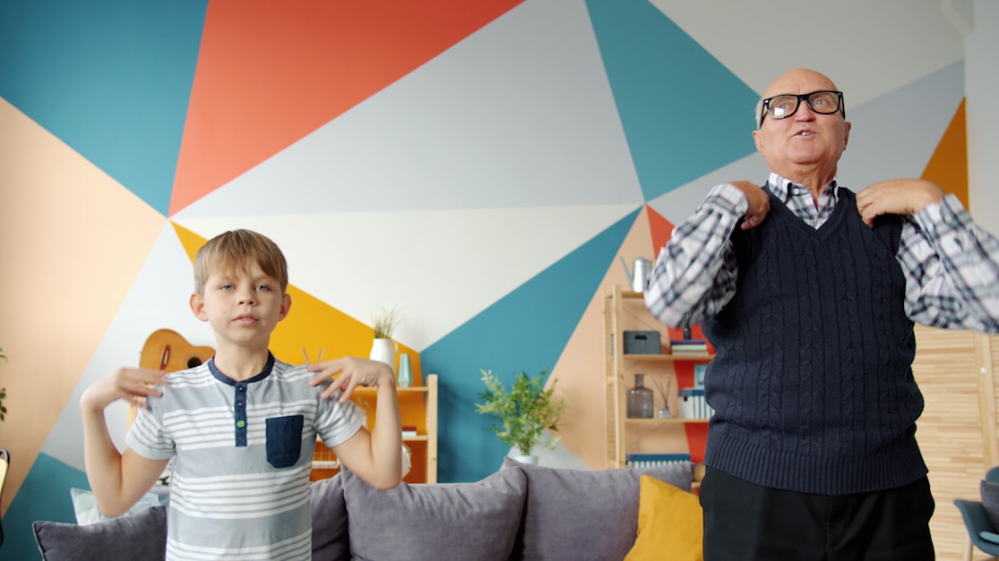 A boy and grandfather making playful gestures against a colourful wall