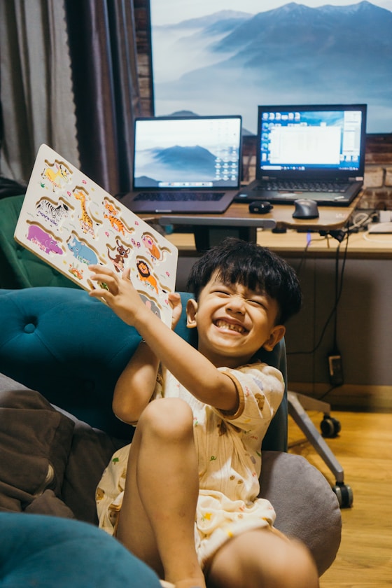 A boy laughing while holding up an animal picture book