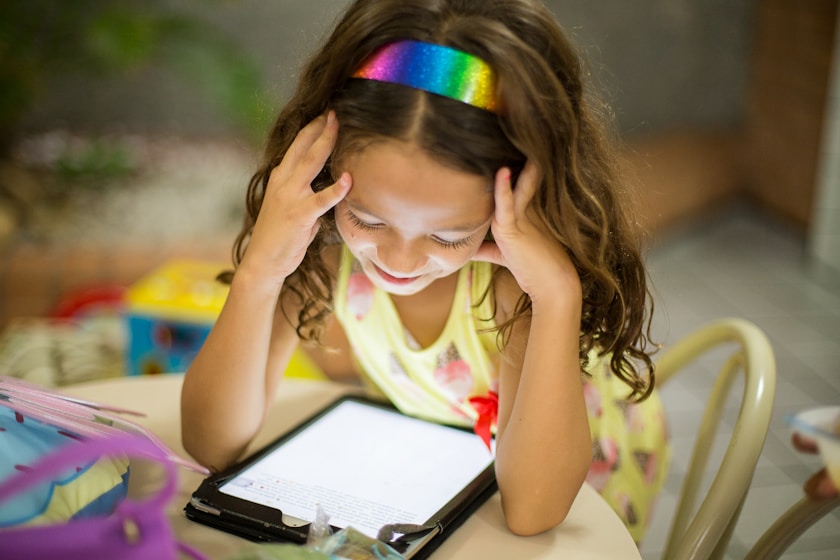 A girl looking at a tablet with her head resting on her hands