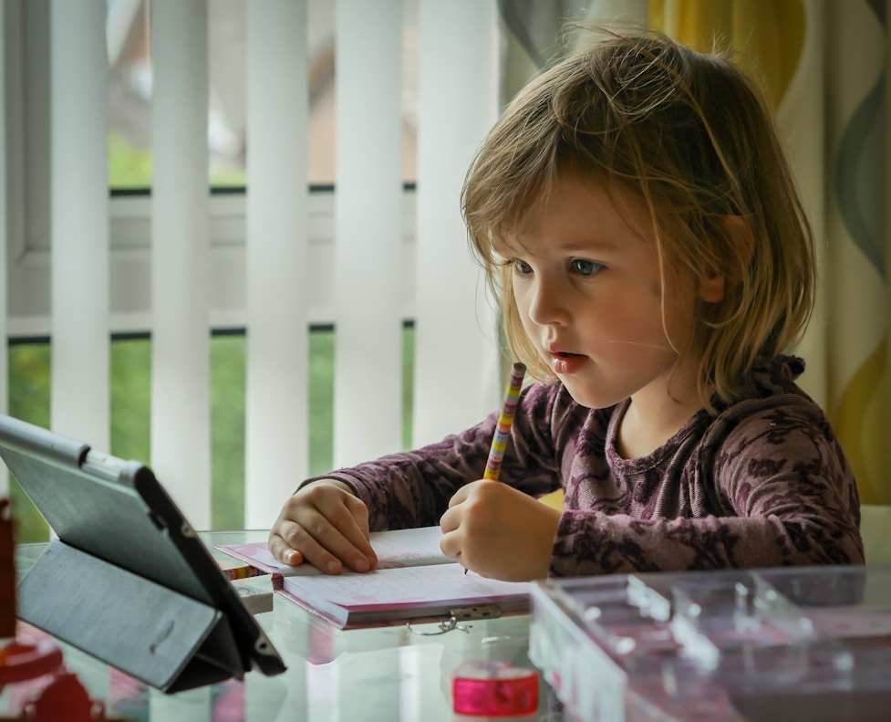 A girl writing in a notebook next to a tablet