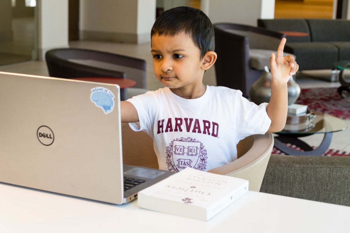A boy raising his hand while sitting at a laptop