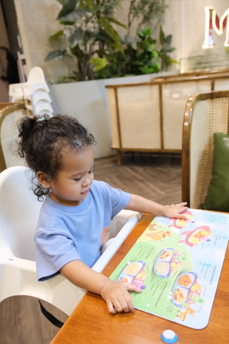 A toddler sitting in a high chair looking at a placemat activity