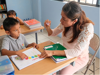 A teacher helping a boy with a colourful workbook at a school desk