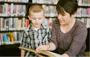 A boy reading a book with a clinician among library shelves