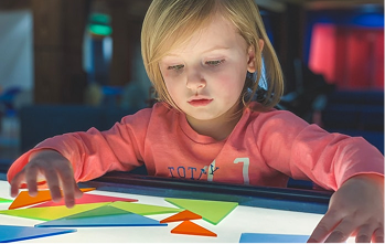 A girl arranging coloured tangram shapes on a light table