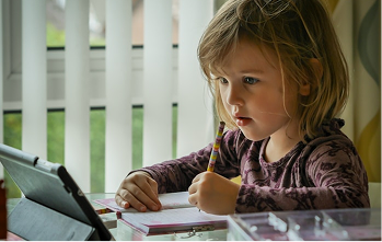 A girl completing schoolwork with a tablet beside her at home
