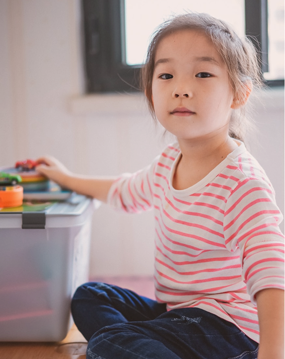 A girl sitting beside a toy storage box, looking at the camera