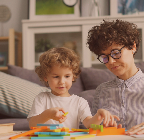 A speech and language therapist playing with building blocks with a young child at Hiba by Anthalora