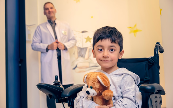 A child in a wheelchair holding a teddy bear, with a doctor nearby at Hiba by Anthalora