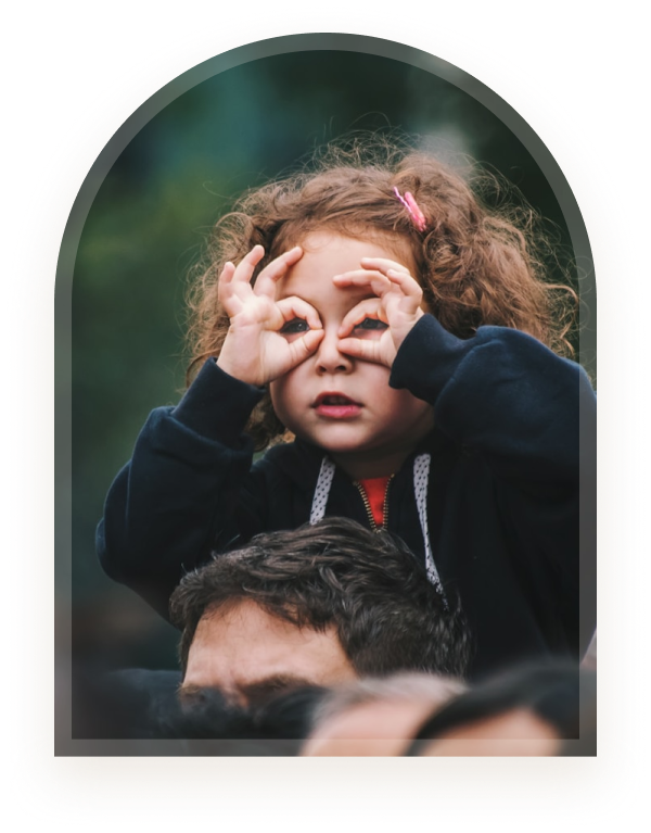 A girl making glasses shapes with her fingers on her father's shoulders