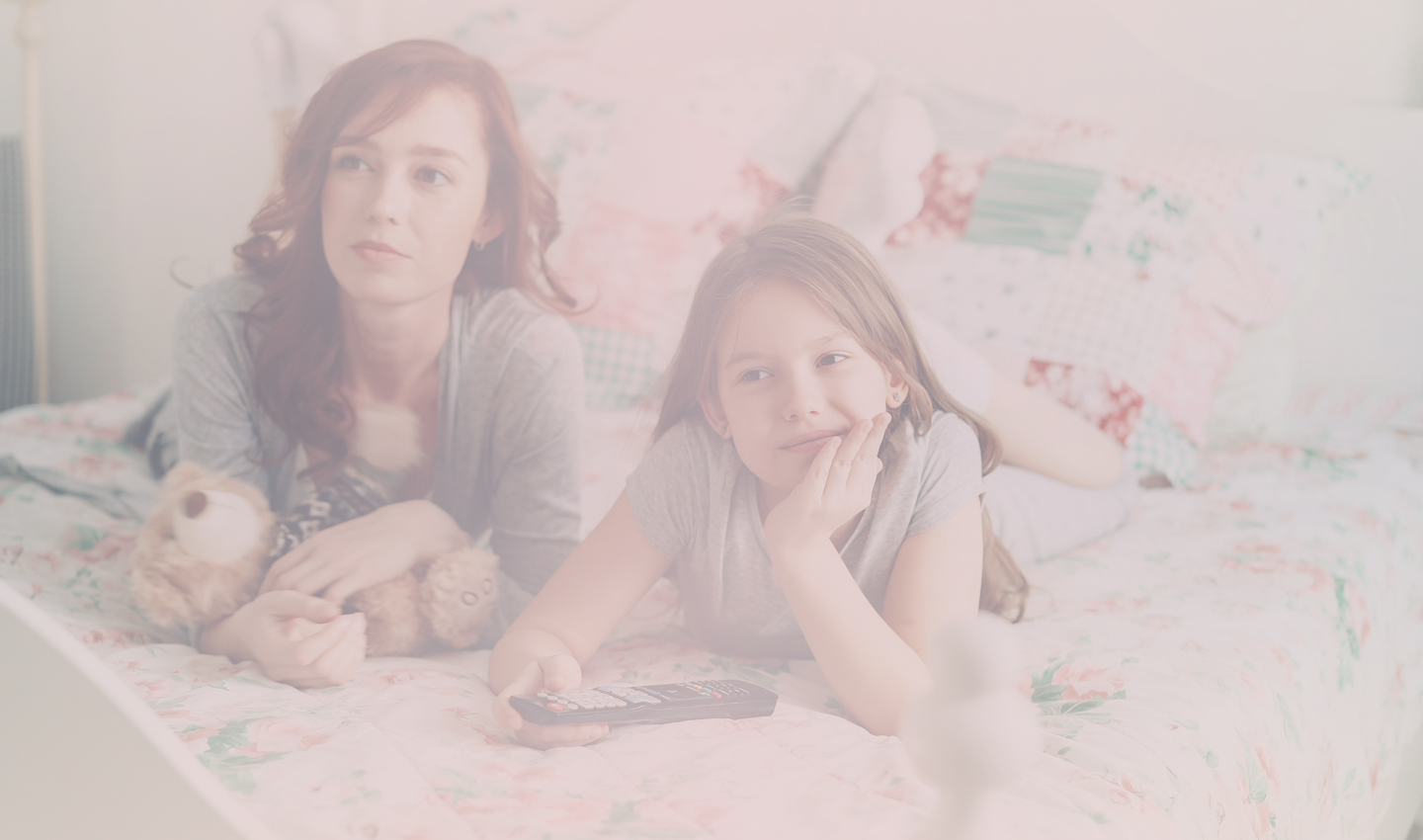 A mother and daughter lying together on a bed watching television